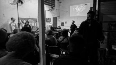 Foto em preto e branco de pessoas assistindo a uma apresentação em sala de aula.
