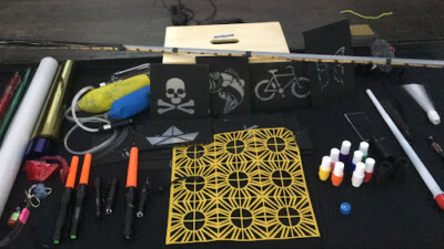 Vários materiais de artesanato, incluindo adesivos, canetas, tintas e outros objetos dispostos sobre uma superfície escura.