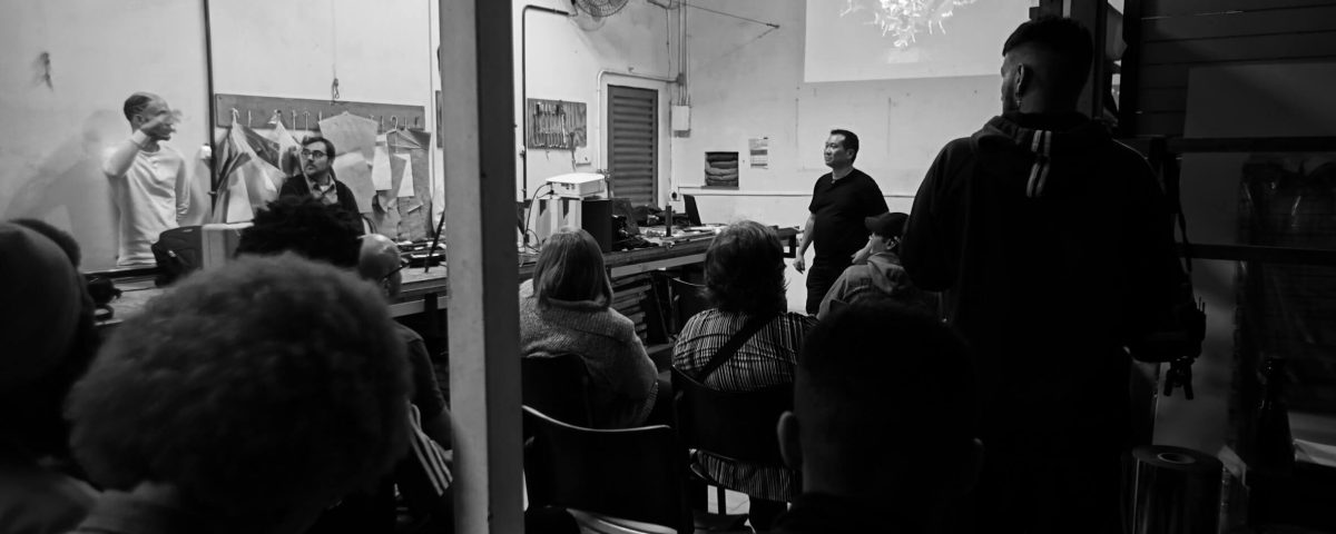 Foto em preto e branco de pessoas assistindo a uma apresentação em sala de aula.